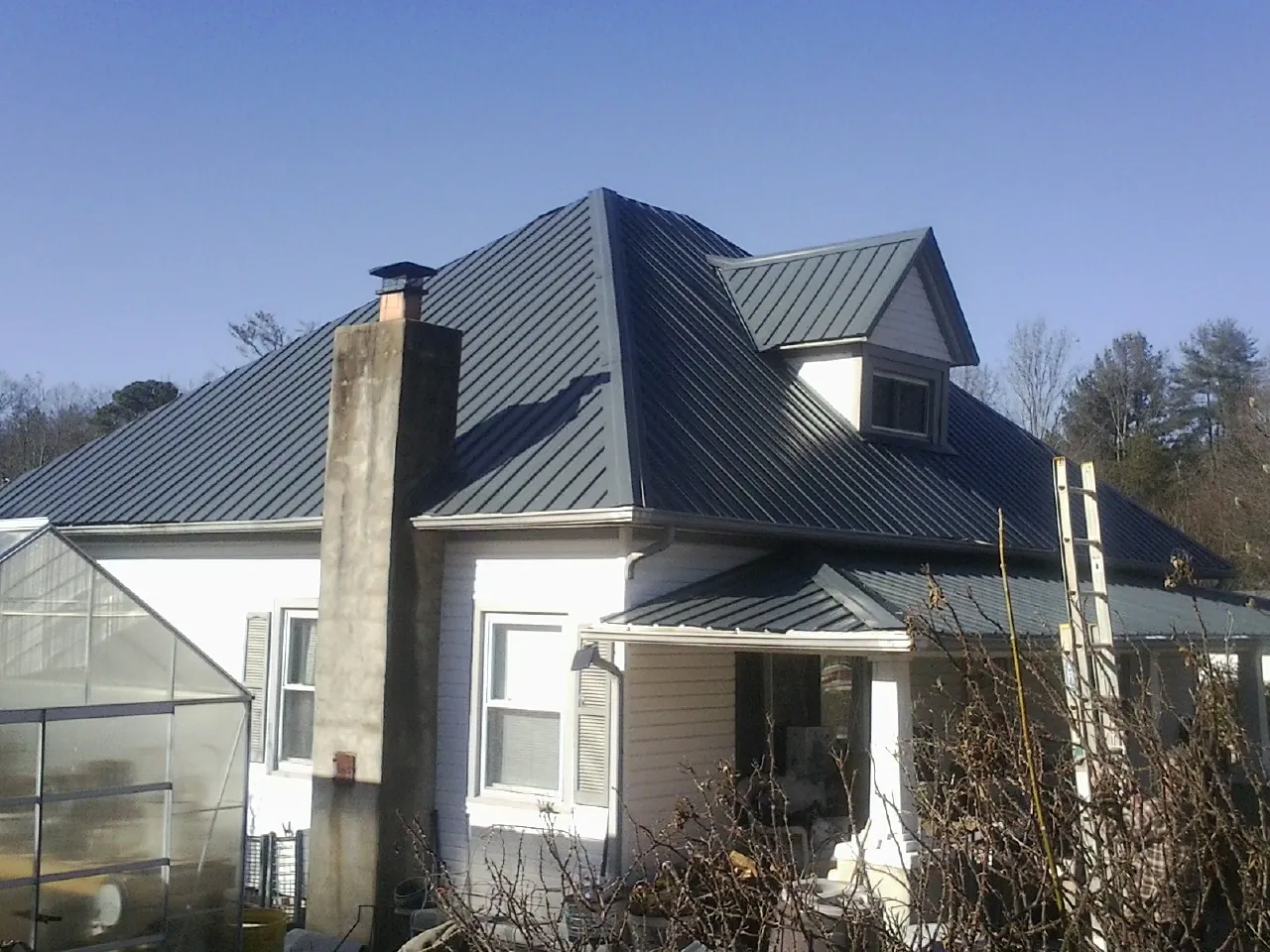 Dark blue standing seam metal roof on a white farmhouse with dormer — Slate & Tile Roof Repair by Roofing Brothers in Dyersville