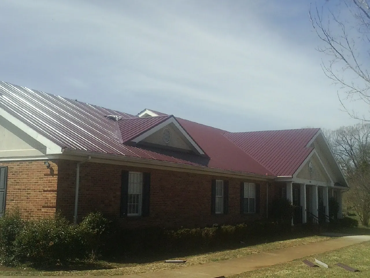 Red metal roof with gabled entries on a long brick building, from a Hail Damage Roof Repair job in Dyersville