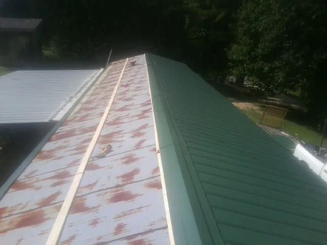 Old rusted panels beside newly installed green metal roofing — Wind Damage Roof Repair by Roofing Brothers in Dyersville