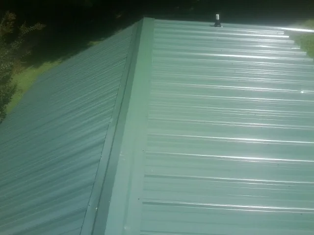 New green metal panels meeting at the ridge of a roof — Flat Roof Repair work by our crew in Dyersville