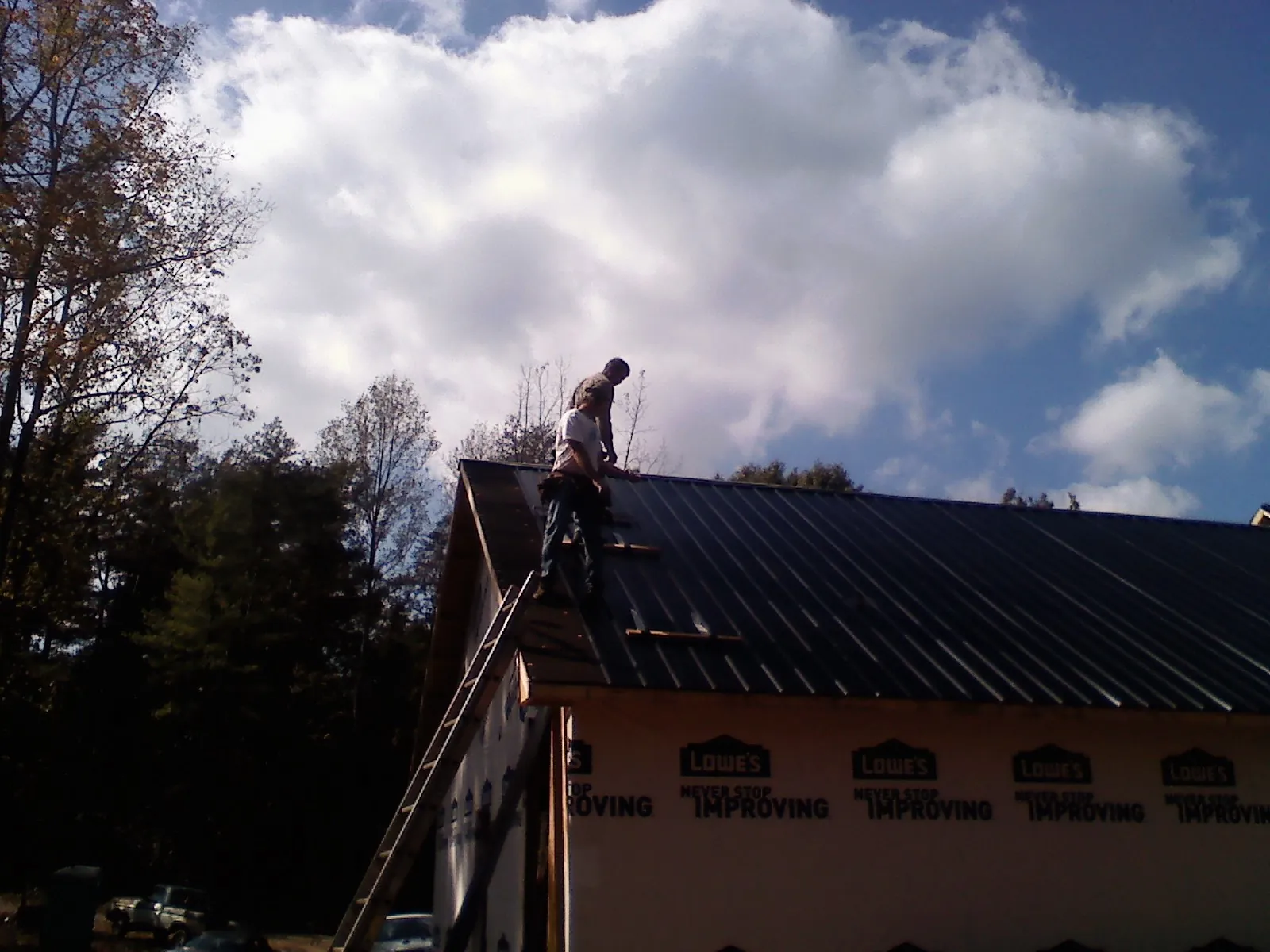 Roofer fastening dark metal panels high against a cloudy sky, from a Roof Inspection job in Dyersville