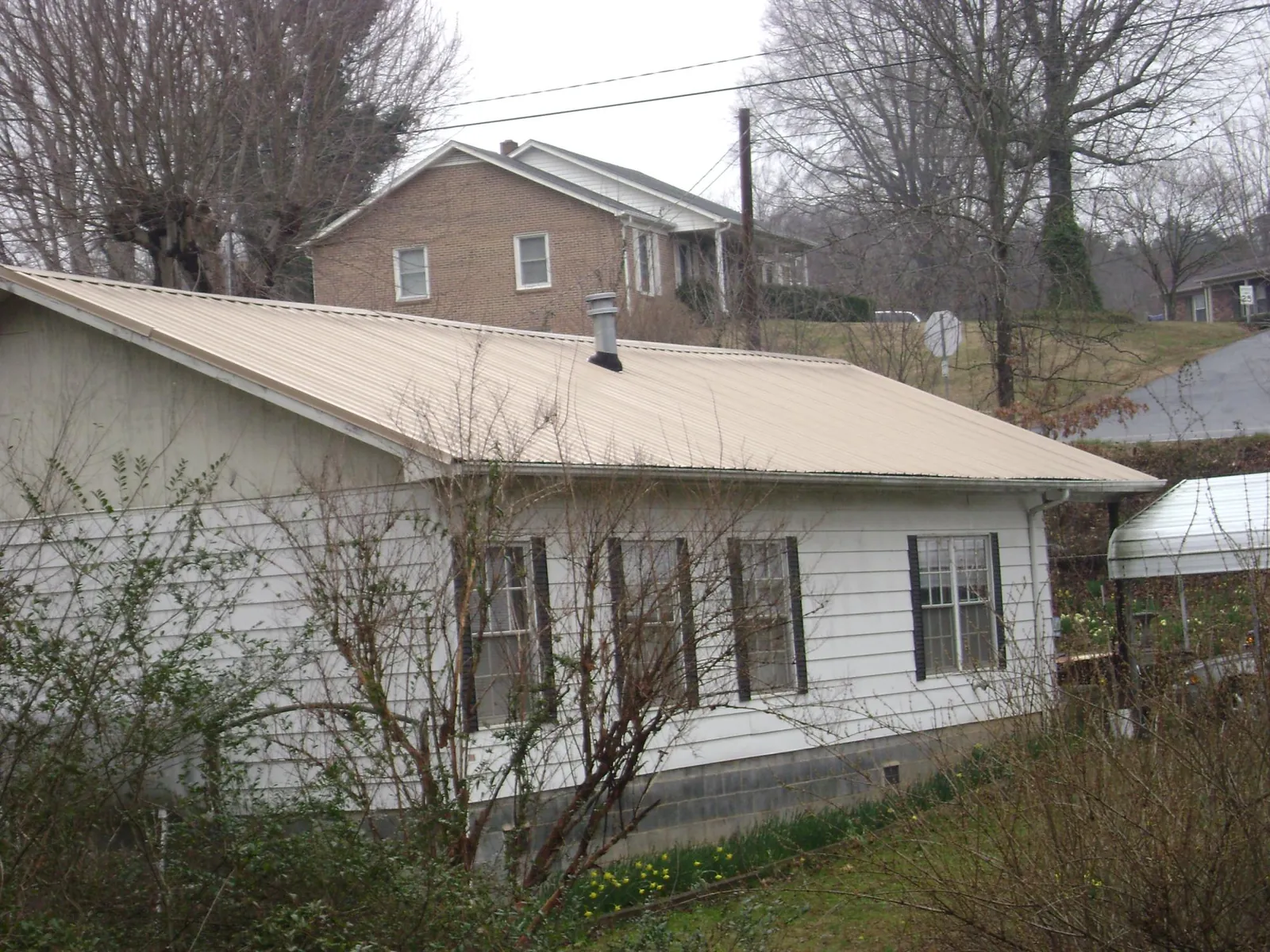 Tan metal roof on a white sided house set into a hillside — Commercial Roofing by Roofing Brothers in Dyersville