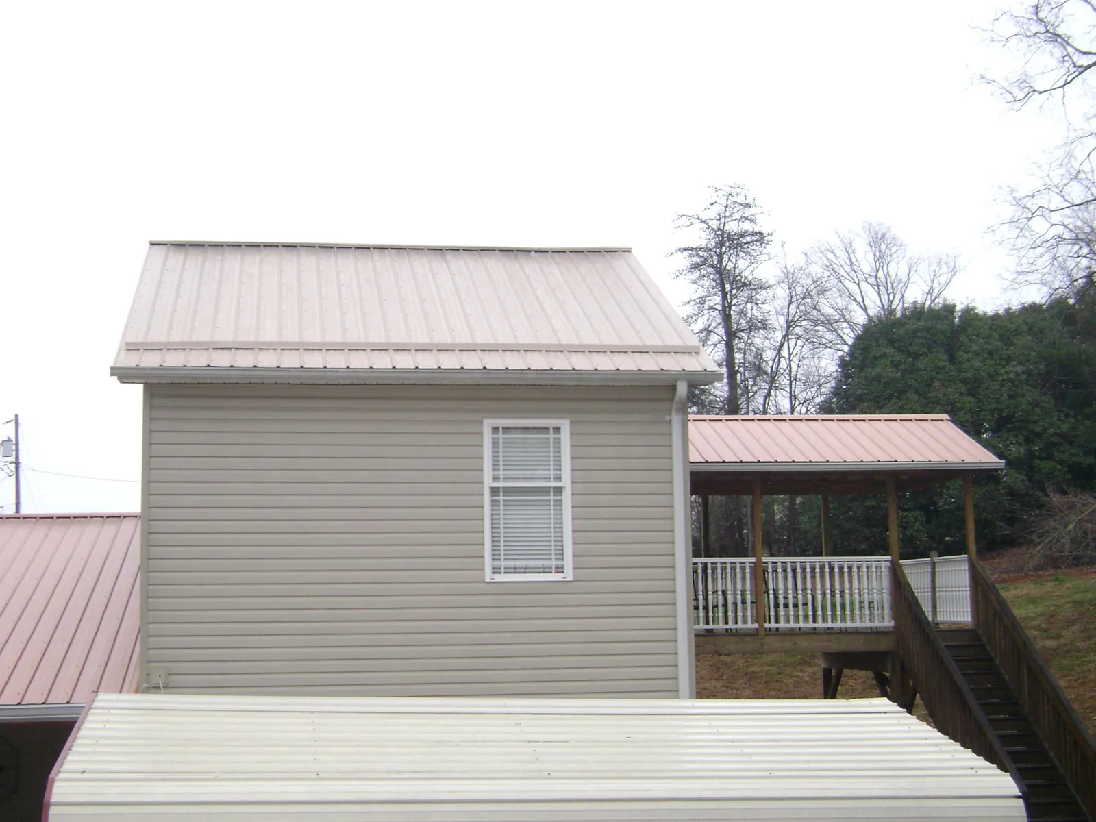 Tan metal roofs on a two story addition and attached porch, from a Roof Replacement job in Dyersville